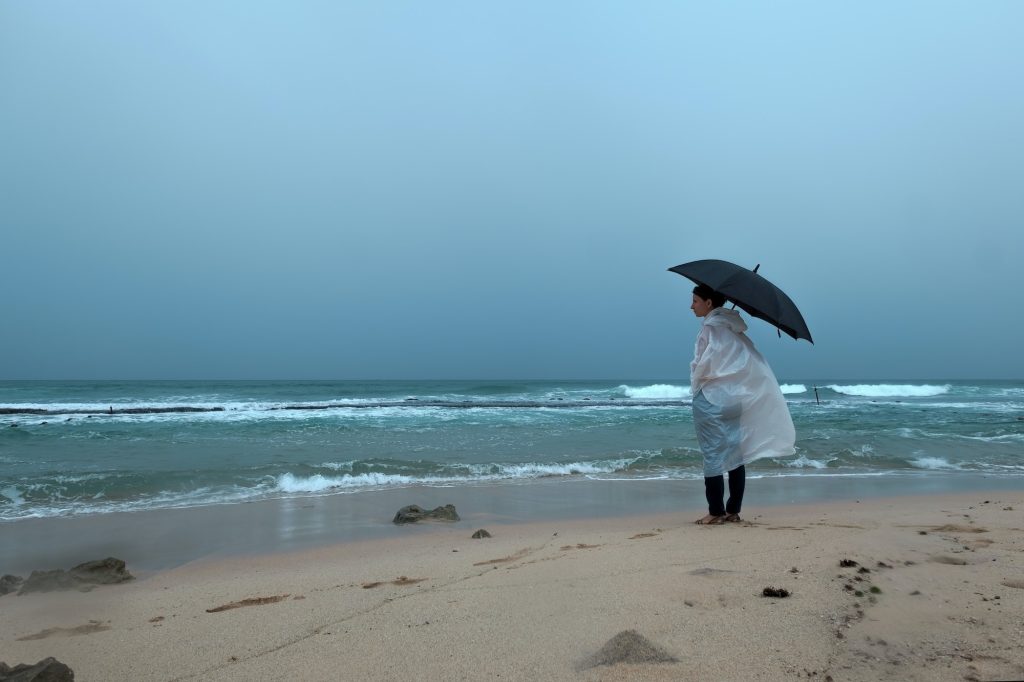 Young woman walking with an umbrella in front of ocean in rainy weather
